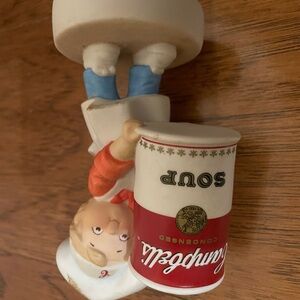 Campbell’s figurine kid delivering large soup can w/ red and white accents